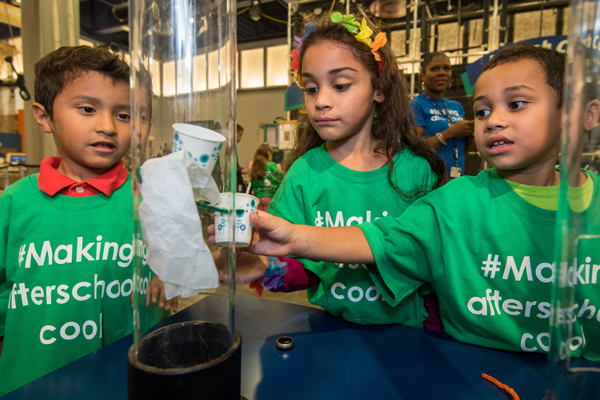  Three children gather around a tube containing a science experiment.